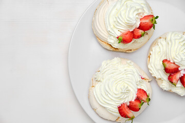 Top view of three Pavlova meringue cakes with fresh strawberry on a white plate on white background with copy space. Homemade pastry.