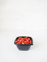 Fresh ripe red wild strawberries in a black plastic container on a white background. Copy space