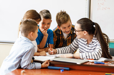 Female teacher helps school kids to finish they lesson.They sitting all together at one desk.