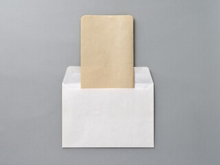 An empty Kraft brown card for an invitation or greeting and a white paper envelope on a gray textured background. Mock-up. Stylized stock photos. The view from the top.