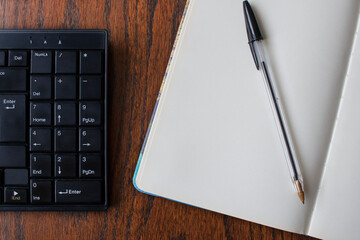 Top down view of computer keyboard, open notebook and pen on wooden desk. Organization, planning and handwriting versus typing concept © Marta Nogueira