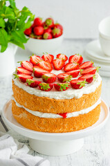 Victoria sponge cake with strawberry jam, whipped cream and fresh strawberries on top on a white plate on a wooden background. Vertical orientation, copy space.