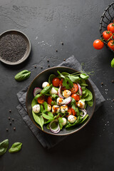 Salad with spinach, summer vegetables and Mozzarella on black background. Top view.