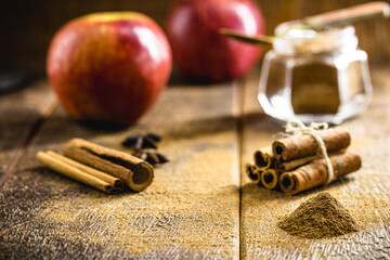 Ground cinnamon, cinnamon sticks, with apples in the background, wooden background in a rustic style. Spot focus.