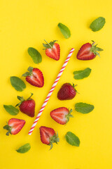 Composition with a cocktail straw, strawberries and mint  on the yellow background. Top view. Location vertical.