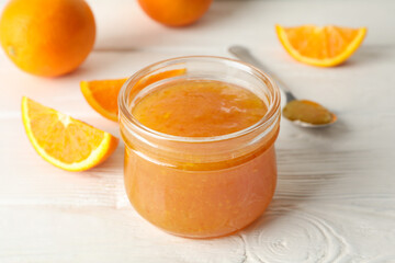 Oranges, spoon and glass jar with jam on white wooden background