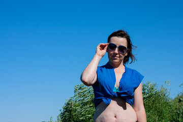 a young sexy woman in a swimsuit and a blue shirt adjusts her sunglasses. in summer