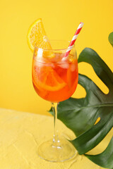 Aperol spritz cocktail and palm leaf on yellow background. Summer drink