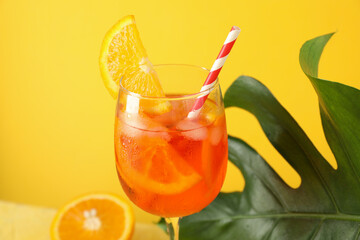 Aperol spritz cocktail and palm leaf on yellow background. Summer drink