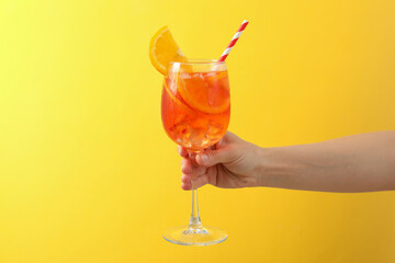 Female hand with glass of aperol spritz cocktail on yellow background