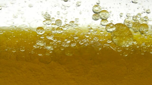 Golden and white background of poured sesame oil and black cumin oil, resulting in air bubbles and bulbs. Close shot of pouring peanut oil and golden walnut oil in container. Close-up of olive oil.