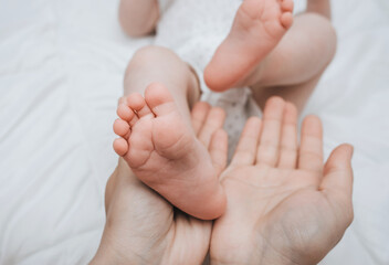 A caring and loving mother holds in her hands the legs and fingers of a small, newborn, sleeping baby on the bed close-up. Woman's happiness. Photography, concept.