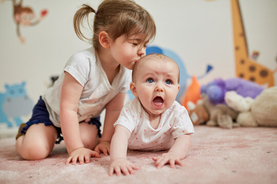 Girl kissing her little sister lying on carpet at home