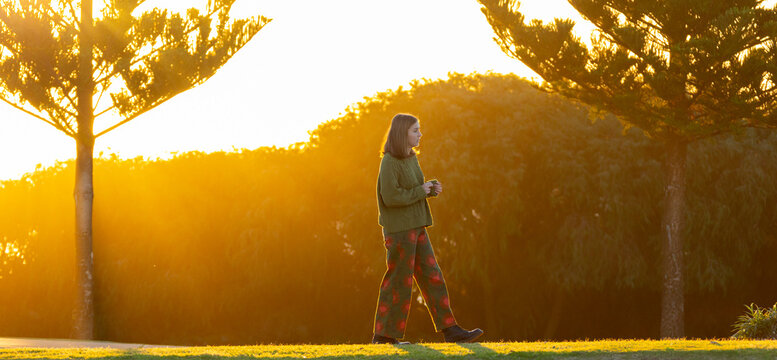 teenager back-lit walking past pine trees in coastal park