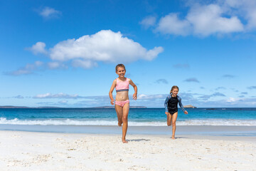 Two kids running up the beach away from the water