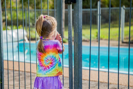 Little Girl Standing Safely Outside Pool Fence Gate Looking In