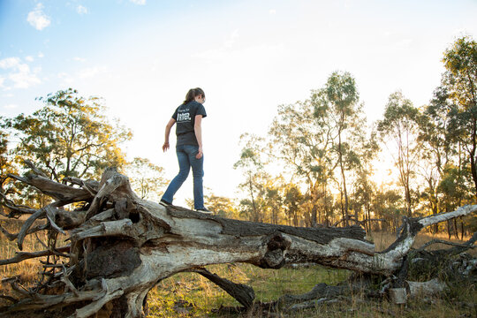 Happy teen girl walking along a fallen tree stump in paddock