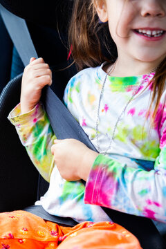 Little girl happily wearing seat belt in booster seat in car