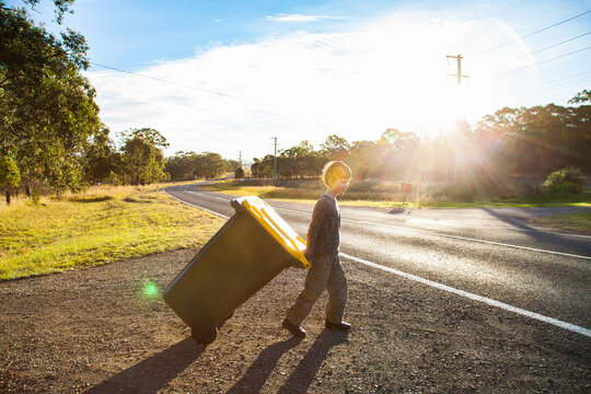 Boy pulling bin on road