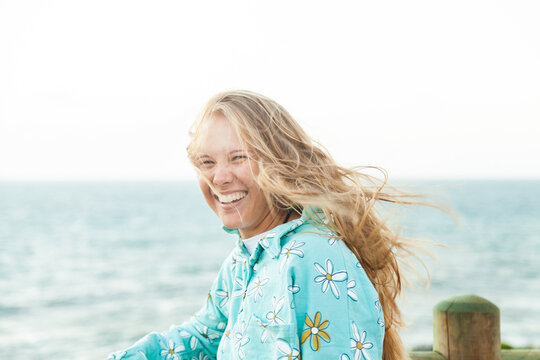 Young adult looking out over the ocean laughing with wind blowing her hair