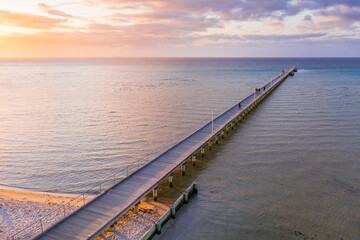 An aerial view of a long narrow jetty jutting out to sea at sunset