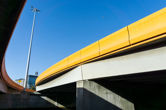 Looking up underneath curved freeway on ramps and a single light pole against a blue sky