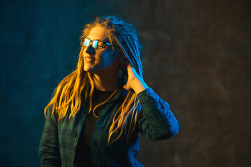 Young woman with dreadlocks in colorful neon lighting. Stylish attractive girl in glasses on dark background.