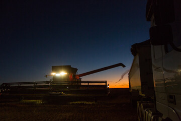 Combine harvester about to unload grain into a semi trailer truck at night