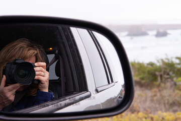 Woman taking a picture of self in car side rear view mirror