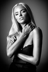 Portrait of blond young woman with beautiful makeup and hairstyle in a black lace dress stands on gray background. Fashion model poses in elegant clothes in studio. Black and white, monochrome