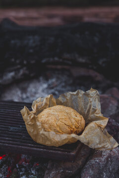 Rustic damper bread in brown baking paper on the red hot coals of a campfire
