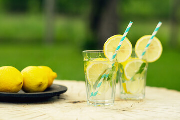 Lemonade with lemon and mint in glass on wooden background. Refreshing summer drink. Drink making ingredients for lemonade.