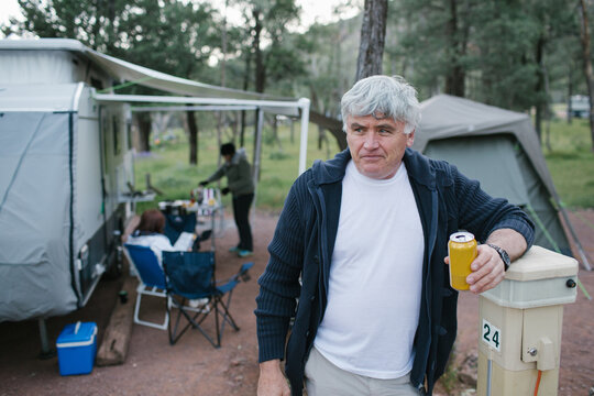 Older Man Standing In Front Of A Caravan And Tent With A Beer