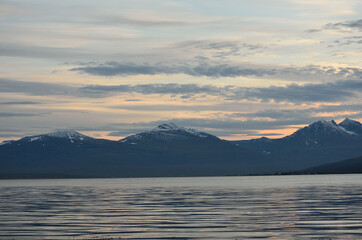 orange vibrant dawn sky over tall mountain with new snow and blue fjord water underneath