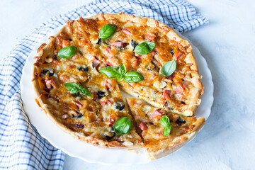 Delicious and crispy pizza with olives and sausages with a cut piece on a light background with a blue napkin, top view, copy space