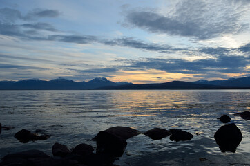 orange dawn sky over majestic mountain with new snow and reflection in the cold fjord water in late autumn