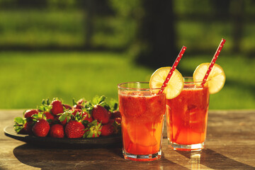 Strawberry lemonade with lemon and strawberries in glass on wooden background. Refreshing summer drink. Drink making ingredients for lemonade. 