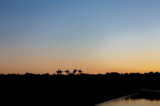 Young surfers walking the rock wall to the waves at dawn