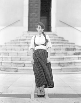 Old fashioned lady wearing a traditional sardinian costume, standing in front of a church entrance in a rural village in Sardinia