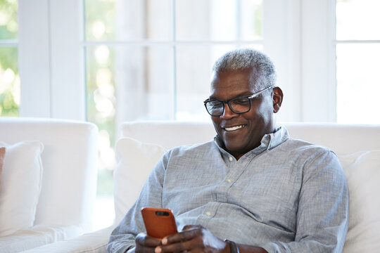 African American Senior man texting on a smart phone sitting on the sofa at home