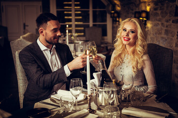 Romance and dating concept. Young couple man and woman with champagne glasses celebrating and toasting in restaurant. Two people male and female in elegant evening suit and dress on romantic dinner