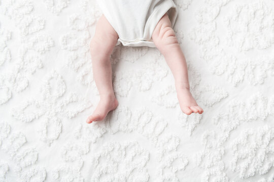A faceless baby laying on a white chenille blanket in a white onesie