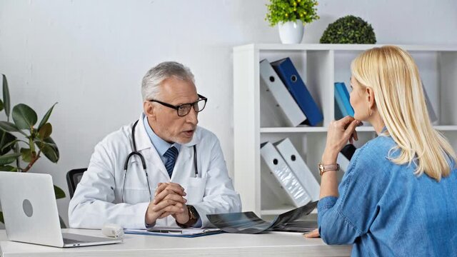 mature doctor looking at x-ray and taking with patient in clinic