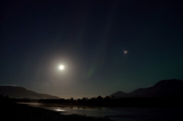 faded aurora borealis on full moon night as the moonlight reflected by the river surface