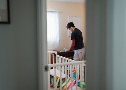 father changes baby diaper in nursery