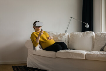 Pregnant woman enjoying VR open a couch