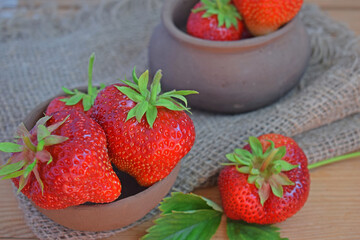 Fresh sweet strawberries in a clay pot on a wooden background.