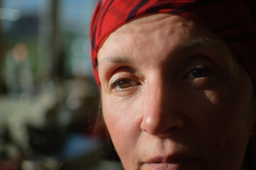 Close-up female portrait of tired mature woman dressed in red clothes and sitting at the end of her work day on sewing machine and cotton bobbins background, tailor profession concept