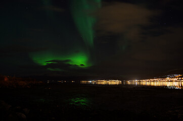 aurora borealis, northern lights over mountain landscape with new snow reflecting on beach sand and fjord water illuminated by the whale island settlement lights in late autumn