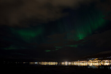 aurora borealis, northern lights over snowy mountain, reflective fjord water and whale island in northern norway in late autumn